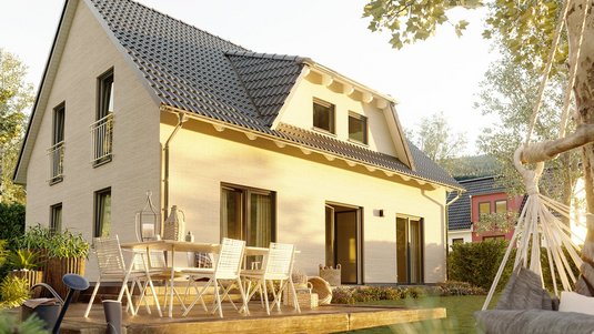 Freistehendes Einfamilienhaus mit grauem Satteldach, heller Fassade und großer Terrasse im Grünen mit Gartenmöbeln.