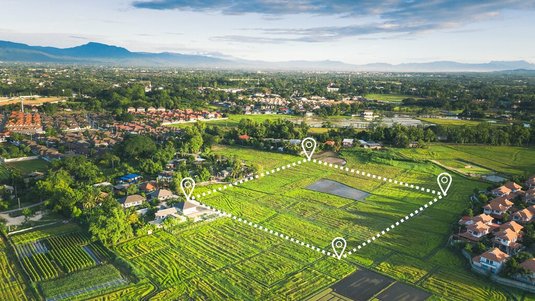 Luftaufnahme eines großen, abgegrenzten Grundstücks im Grünen mit markierten Grundstücksgrenzen, umgeben von Feldern, Wohnhäusern und einer Siedlung.