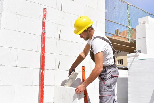 Handwerker beim Mauern mit Porenbetonsteinen auf einer Neubau-Baustelle.