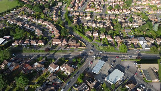 Luftaufnahme eines dicht bebauten Stadtviertels mit vielen Wohnhäusern, Straßenkreuzungen, Kreisverkehr, Grünflächen und einzelnen Gewerbegebäuden.