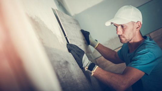 Handwerker trägt Schutzkleidung und verputzt eine Innenwand mit einer Glättkelle während der Ausbauarbeiten im Haus.