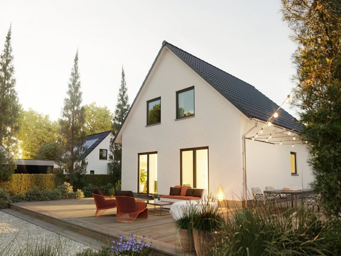 Modernes zweigeschossiges Einfamilienhaus mit Satteldach, großer Holzterrasse, Sitzmöbeln und Beleuchtung im Garten bei Abendstimmung.
