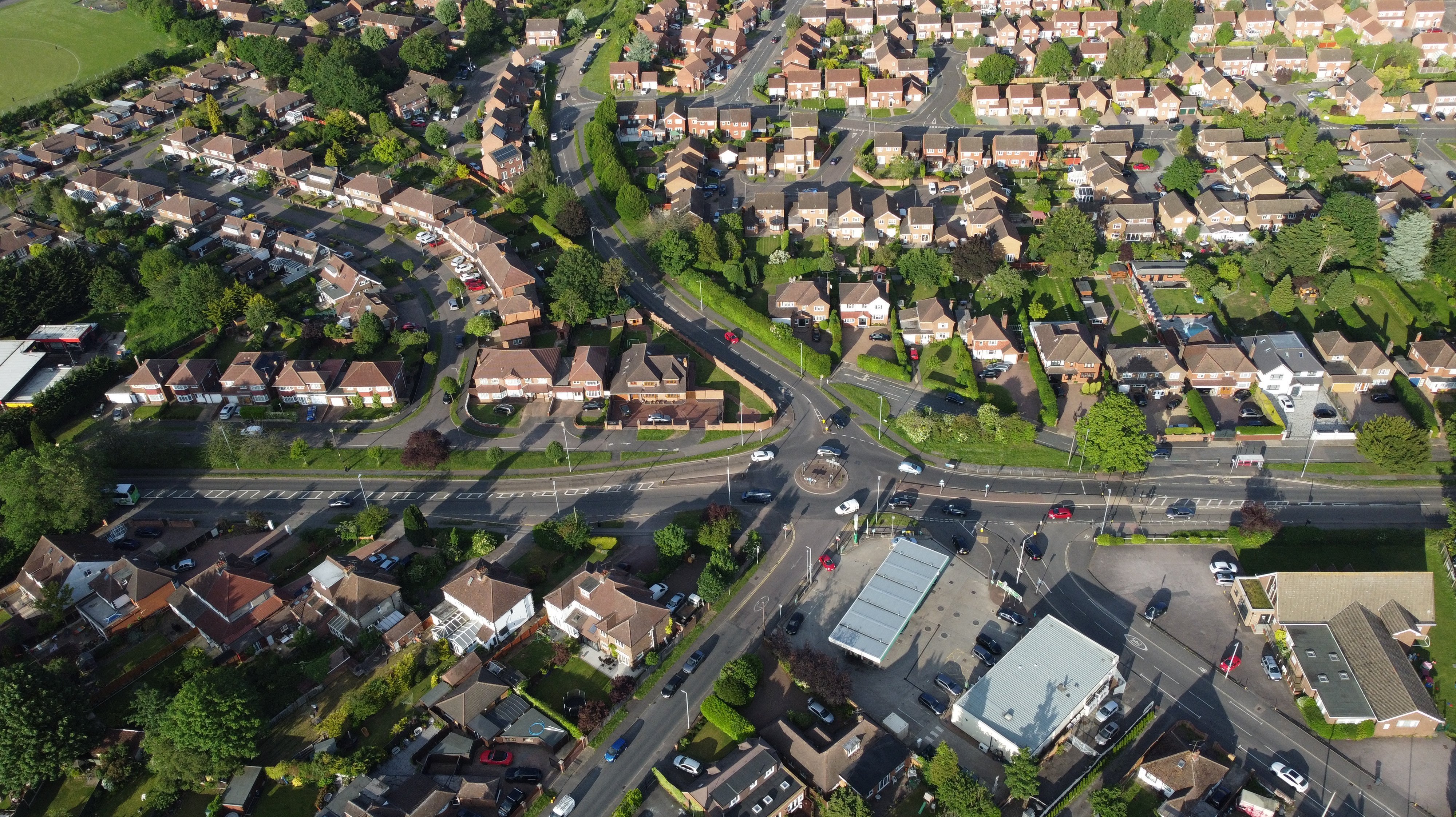 Luftaufnahme eines dicht bebauten Stadtviertels mit vielen Wohnhäusern, Straßenkreuzungen, Kreisverkehr, Grünflächen und einzelnen Gewerbegebäuden.