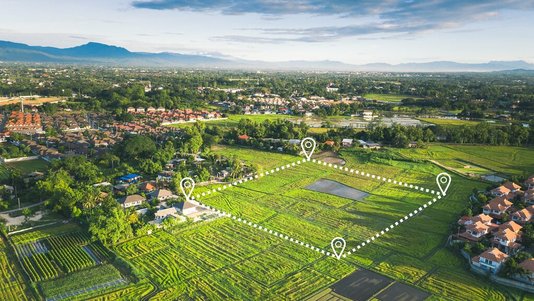 Luftaufnahme eines großen, abgegrenzten Grundstücks im Grünen mit markierten Grundstücksgrenzen, umgeben von Feldern, Wohnhäusern und einer Siedlung.