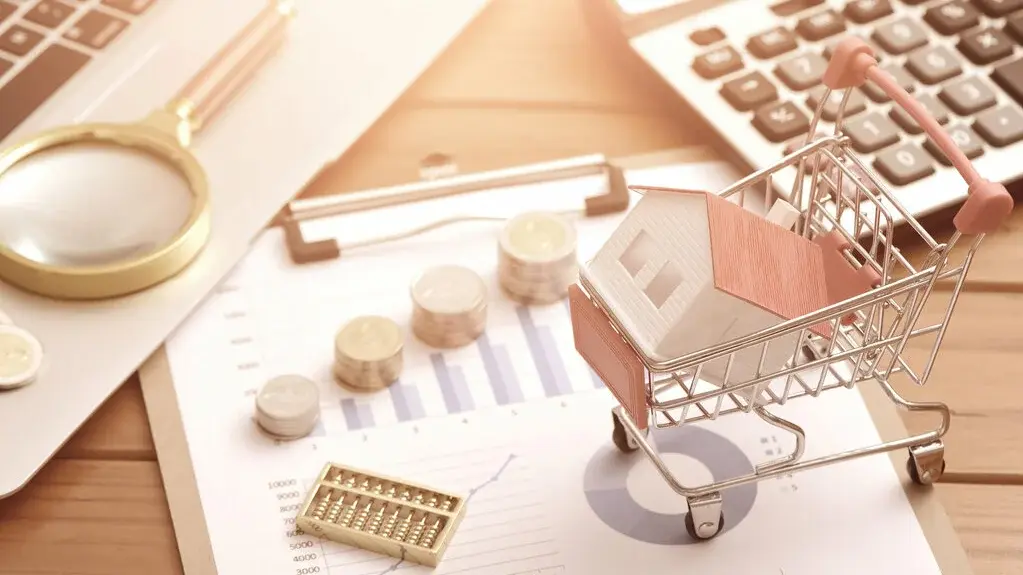 Miniaturhaus im Einkaufswagen auf Finanzunterlagen mit Diagrammen, Münzen, Taschenrechner und Lupe auf einem Schreibtisch.