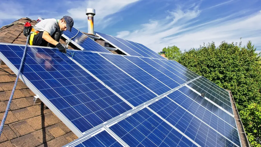 Handwerker installiert Solarmodule auf dem Dach eines Hauses bei sonnigem Wetter.