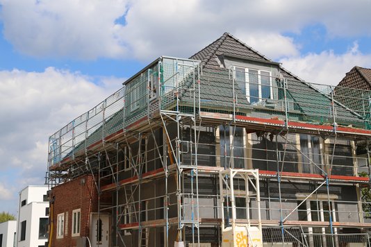 Ein mehrstöckiges Wohngebäude ist vollständig eingerüstet, während an Fassade und Dach im Rahmen einer Sanierung gearbeitet wird.