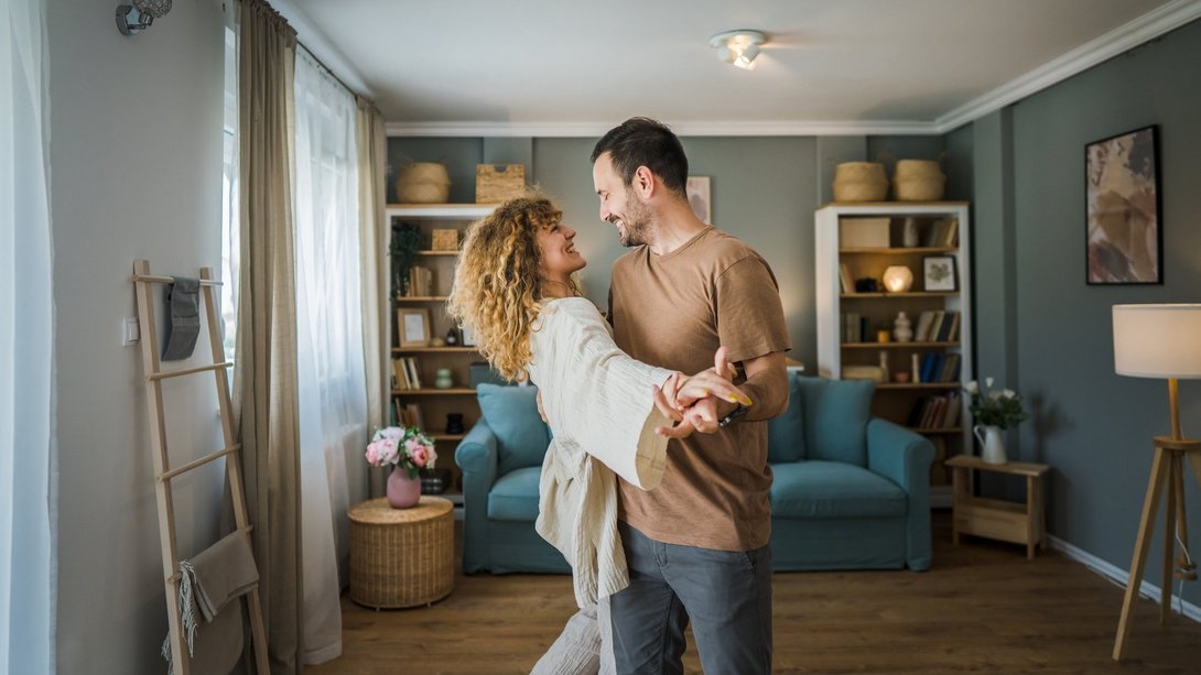 Paar tanzt glücklich im Wohnzimmer seines neuen, gemütlich eingerichteten Zuhauses