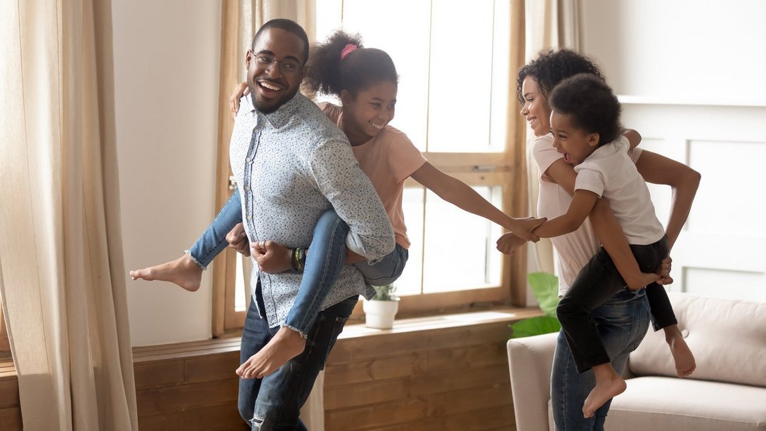 Familie mit zwei Kindern spielt und lacht gemeinsam im hellen Wohnzimmer ihres Zuhauses.